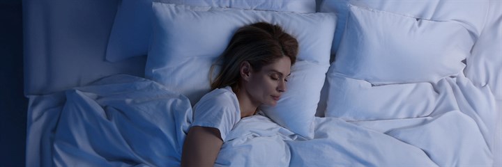 Young woman asleep in bed with white pillows and duvet