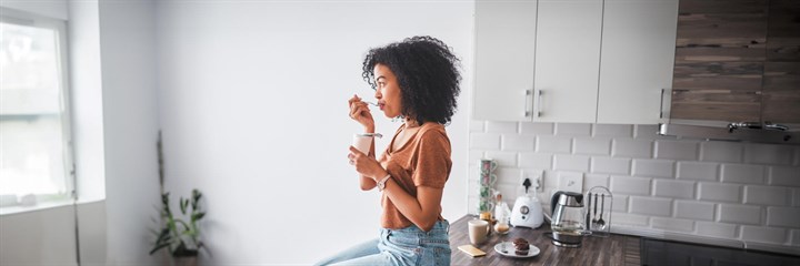 Young woman eating yoghurt on her kitchen counter