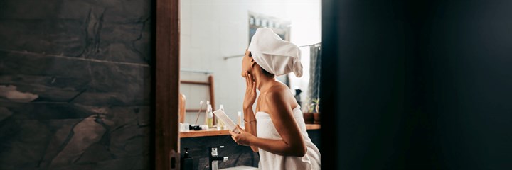 Woman using skincare products looking into mirror