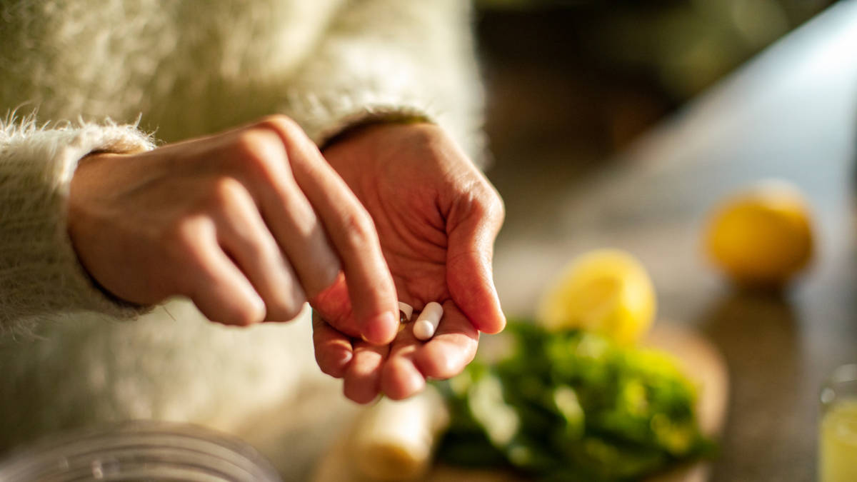 Person holding supplement tablets in kitchen next to food